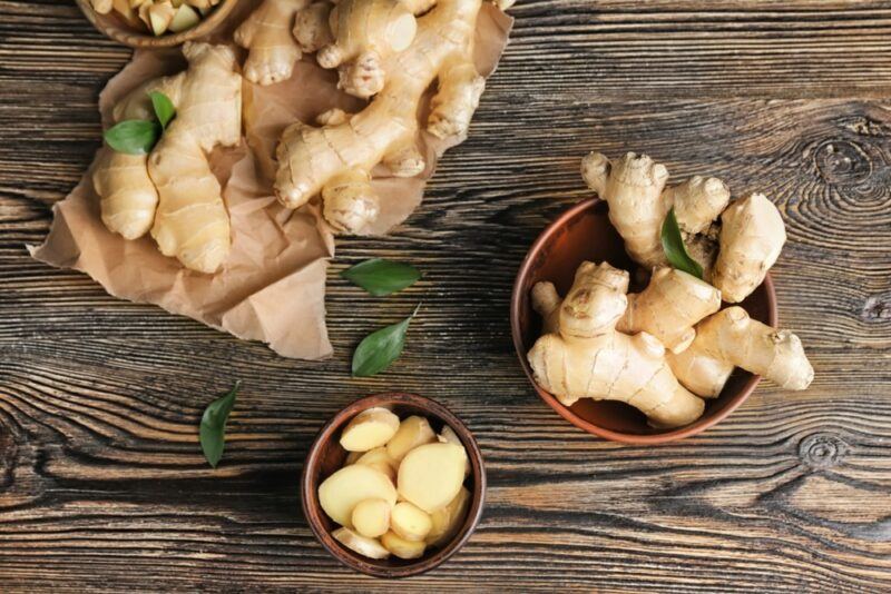 Fresh ginger root on a wooden table and in small bowls, including a bowl of ginger root slices