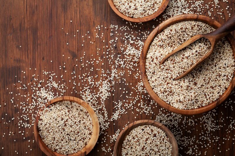 A wooden table with quinoa scattered across it, with three small bowls of quinoa and one large one.