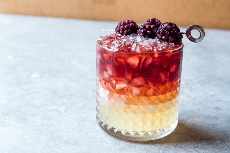 A bramble cocktail on a marble table with blackberries on top