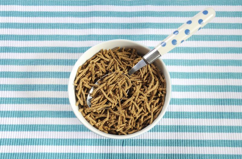 A white bowl that contains a shredded bran cereal with a spoon, on top of a blue and white striped backdrop