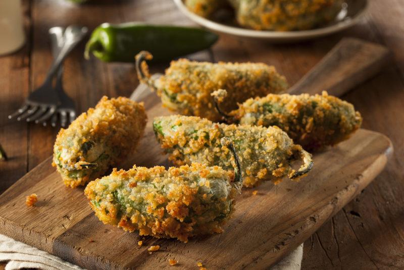 A wooden board with breaded jalapeno poppers