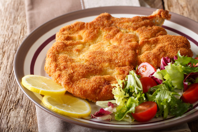 A plate of breaded veal cutlets with a small salad and some lemon slices