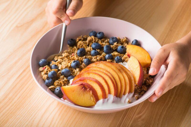 A breakfast bowl with cereal, blueberries, and sliced peaches