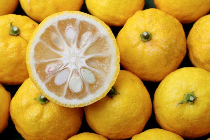 A collection of bright yellow yuzu fruits in a pile, with one that's been cut in half