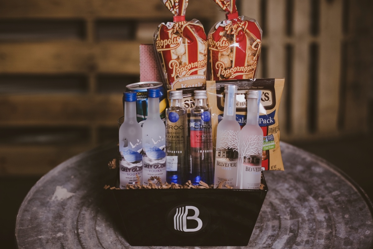 Open top black gift box with 6 sampler bottles of vodka 2 Grey Goose, 2 Ciroc, and 2 Belvedere. In the back of the basket are two single serve bags of popcorn, two bags of pretzels, and a can of sprite