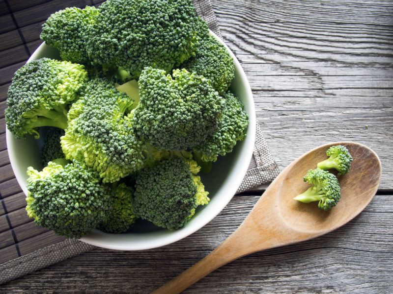 A white bowl and a wooden spoon with broccoli