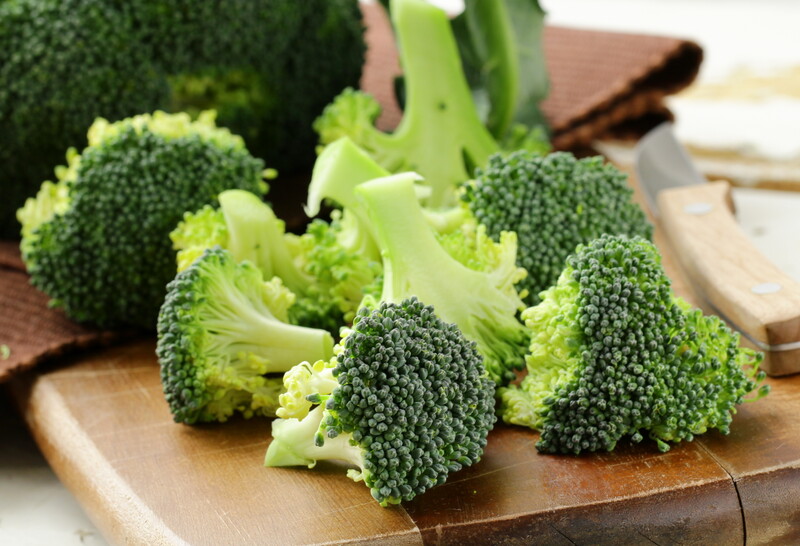 This photo shows broccoli on a wooden cutting board near a knife with a wooden handle.