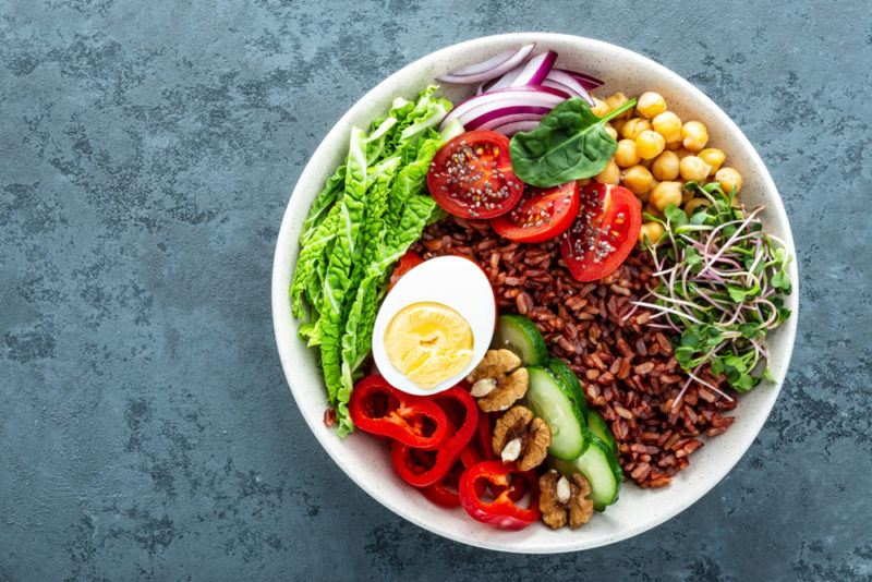 A large white bowl with brown rice, veggies and an egg