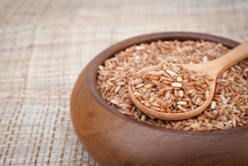 A wooden bowl of brown rice with a spoon