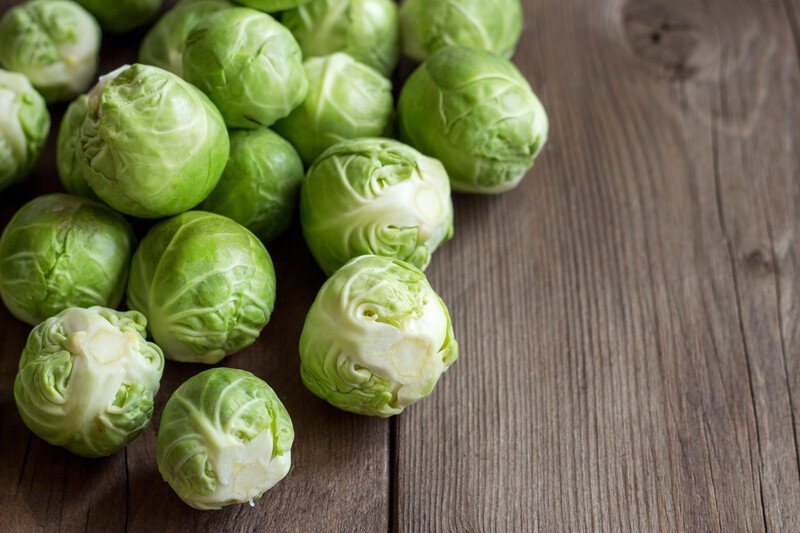 This photo shows several green brussels sprouts on a wooden table.