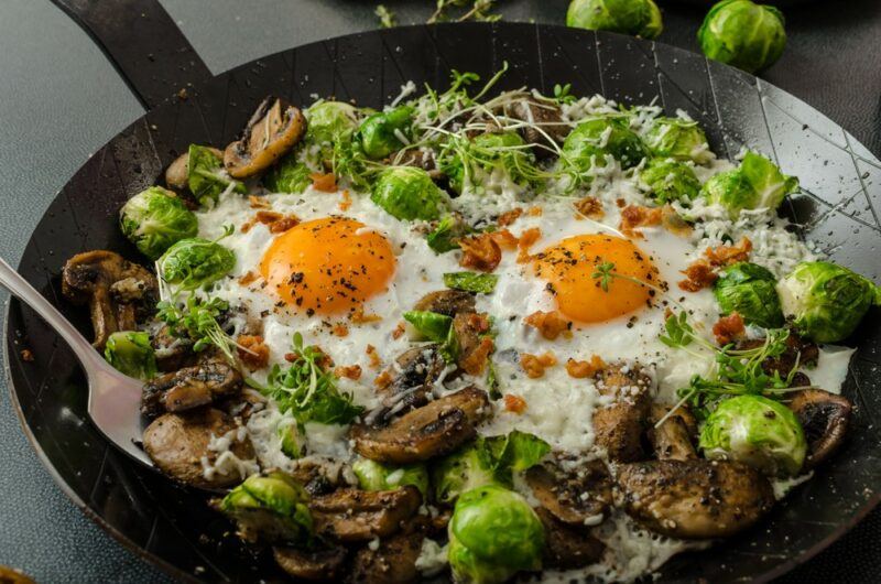 A black fry pan containing brussel sprouts, eggs, and various other ingredients