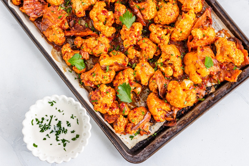 Buffalo cauliflower bites on a sheet pan next to some dip