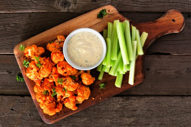 A wooden board with buffalo wings, celery sticks, and dip