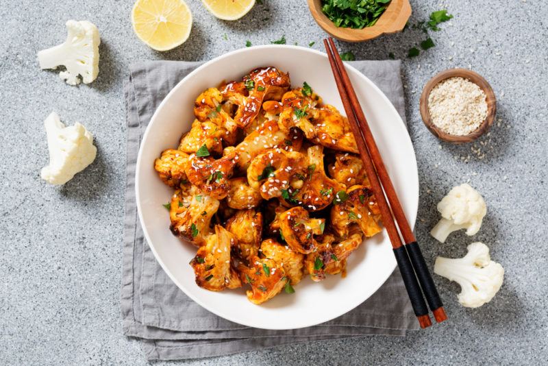 A white plate with buffalo wings made from caulfilower, chopsticks, and pieces of cauliflower scattered around