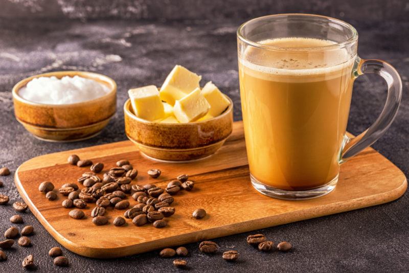 A glass mug of bulletproof coffee next to coconut oil, butter, and coffee beans