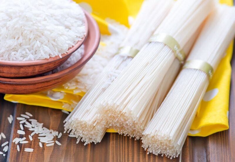 Three bundles of straight rice noodles, next to a bowl of rice