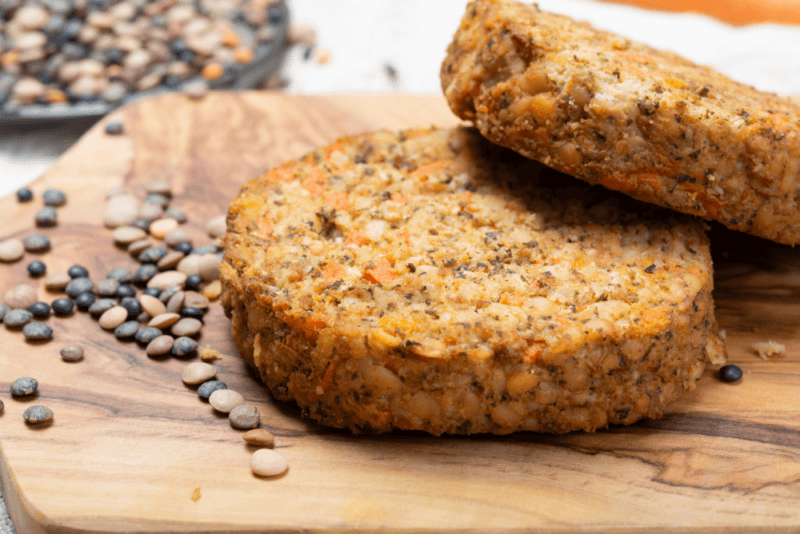 A wooden board with two burger patties that have been made using lentils, plus some raw brown lentils. 