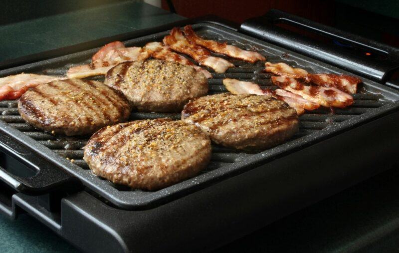 A black smokeless grill with burger patties and bacon