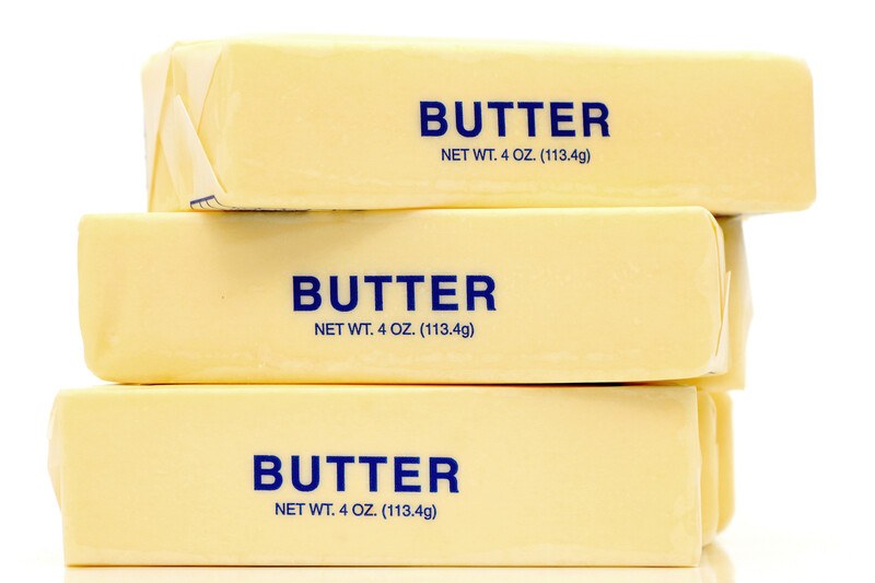 Three cubes of yellow butter in translucent wrappers with blue lettering are stacked on top of each other against a white background.