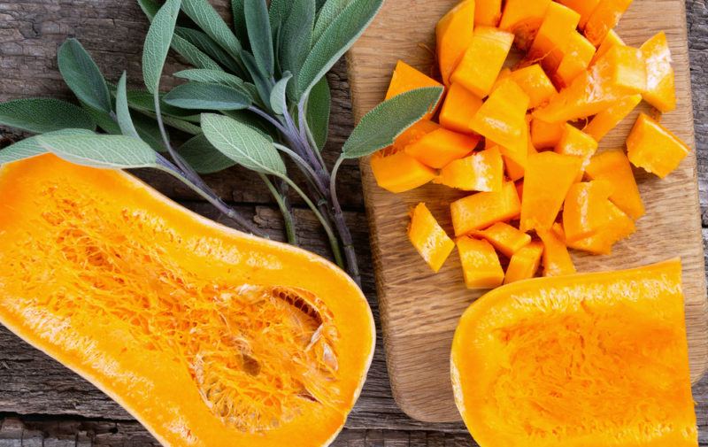 A cooked butternut squash sliced in half with cubes of butternut squash on a board