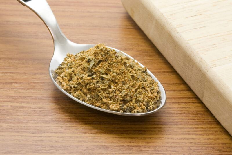 on a wooden surface is a silver spoon full of Cajun seasoning beside a partial image of a wooden board