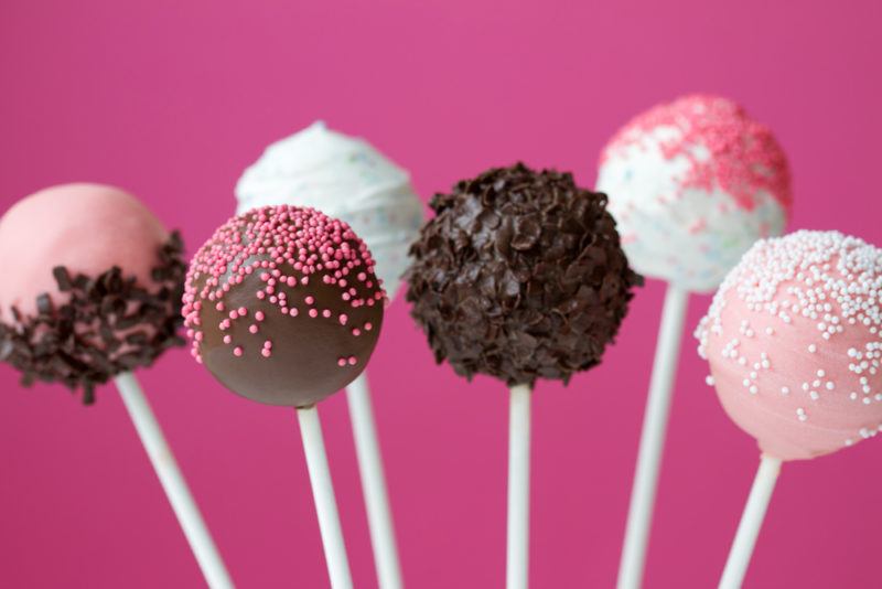 Six cake pops on sticks against a pink background