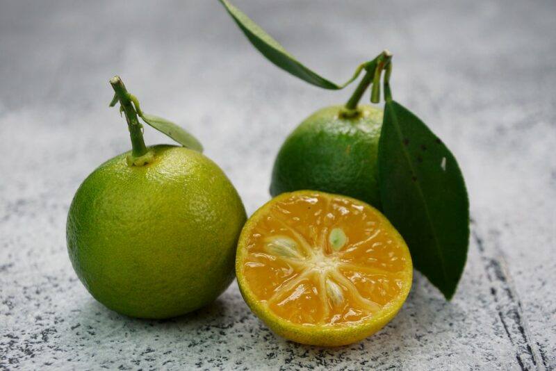 Two whole calamodin fruits on a table and one half