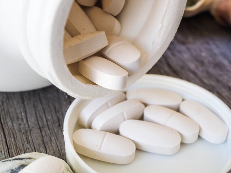 A bottle of calcium supplements, with some more pills on the lid, against a wooden table