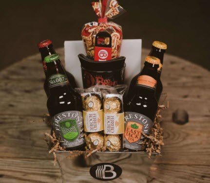 Metal box containing 4 bottles of beer, some chocolates and popcorn on a wooden table. 