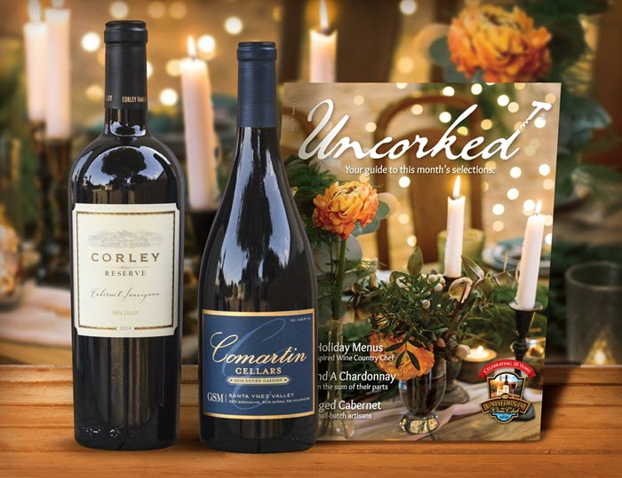 A wooden table with 2 bottles of wine and a magazine