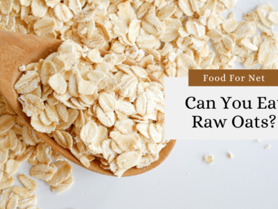 A wooden spoon containing raw oats, with more raw oats on the table, looking at the question of - can you eat raw oats?