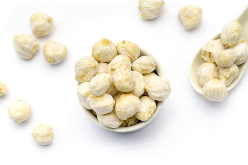 Candlenut | Food For Net A white bowl of candlenuts, with more scattered on the table