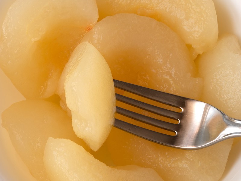 This photo shows an overhead view of canned pears, with one pear slice on a silver fork.