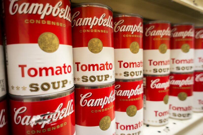 Red and white cans of Campbell's Condensed Tomato Soup stacked two high on a grocery store shelf