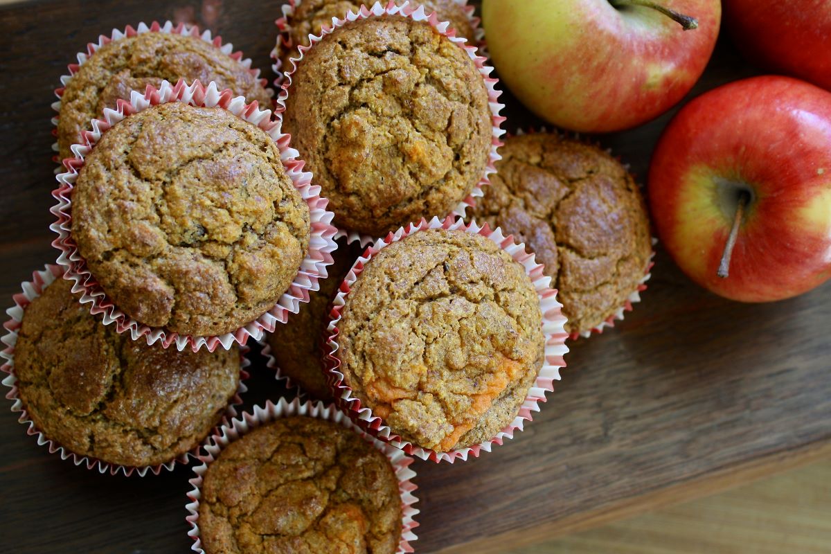 Homemade apple muffins in white and red striped paper muffin liners, in the upper right corner are three fresh red apples.