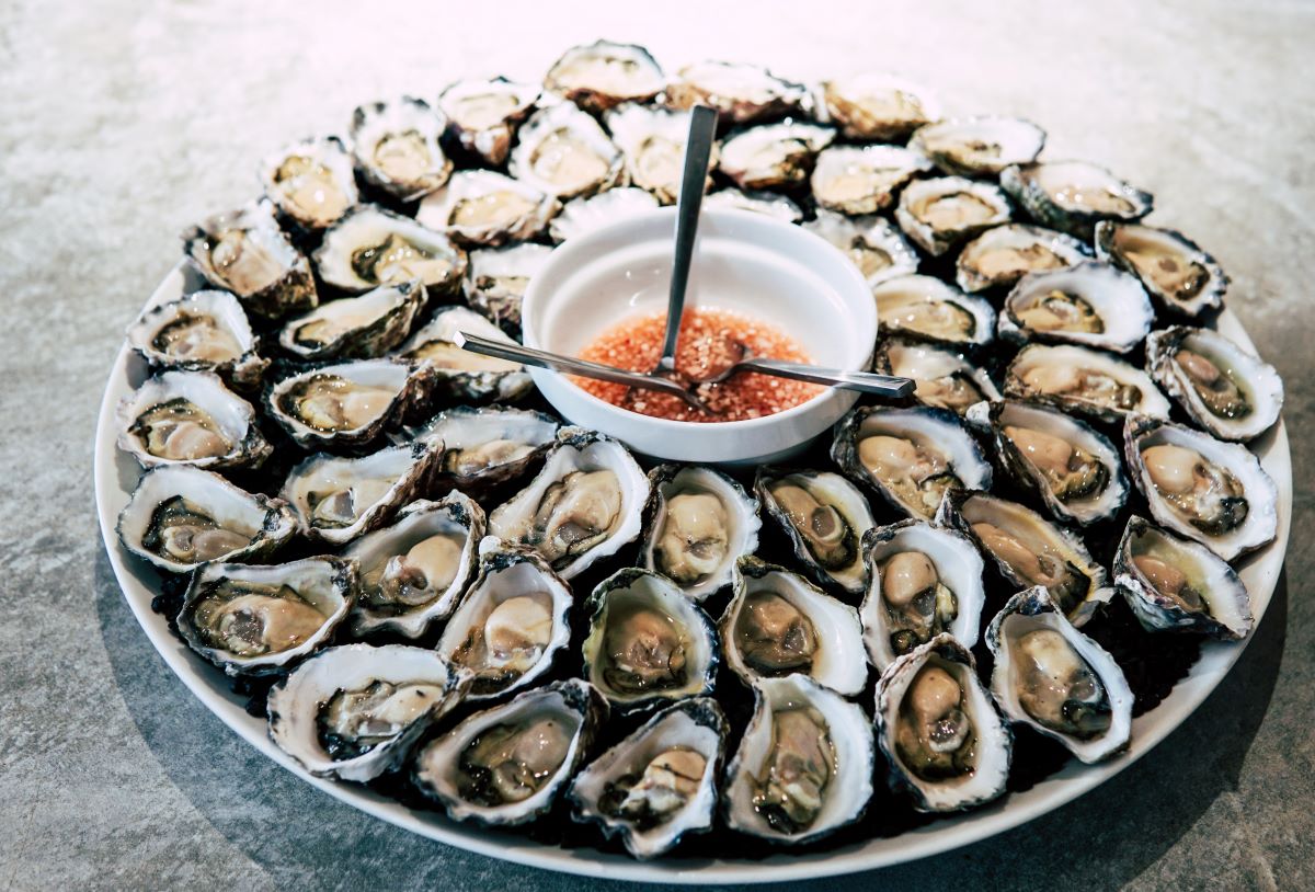 Oyster of the month club - Platter full of raw oysters on the half shell with red wine vinegar sauce in the middle,
