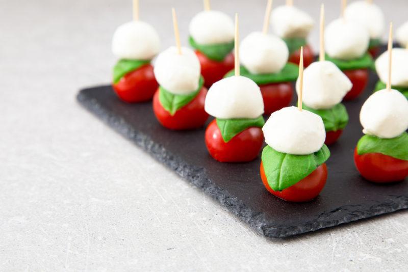 A black slate board with small skewers of tomato, basil, and mozarella cheese