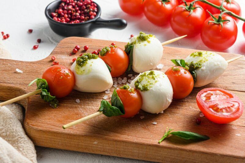 A wooden board with two caprese salad skewers