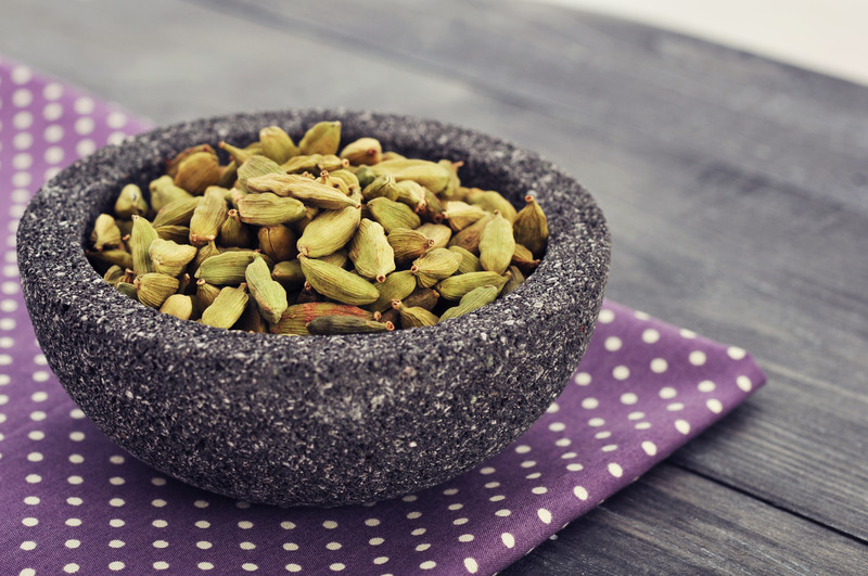 a stone bowl resting on a purple polka dot place mat on a wooden table full of cardamom seeds.