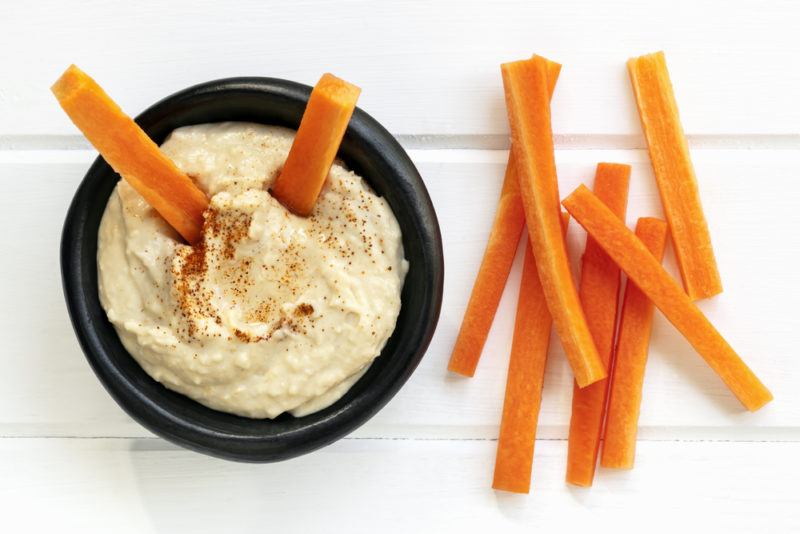 Carrot sticks on a white table with a bowl of hummus