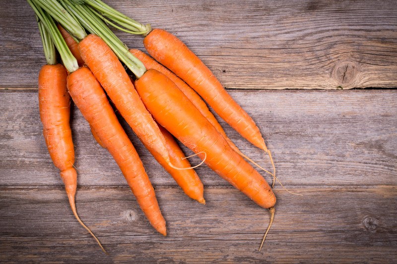 A bunch of seven orange carrots rests on a rustic wooden table.