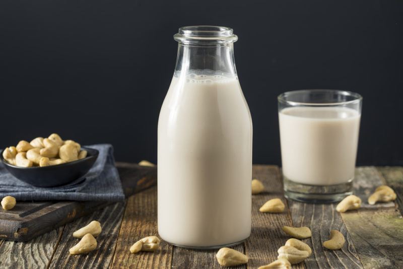 A bottle and a glass of cashew milk next to a bowl of cashews