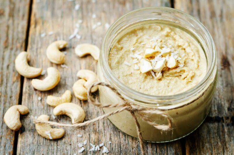 A glass container of cashew butter, next to some raw cashews