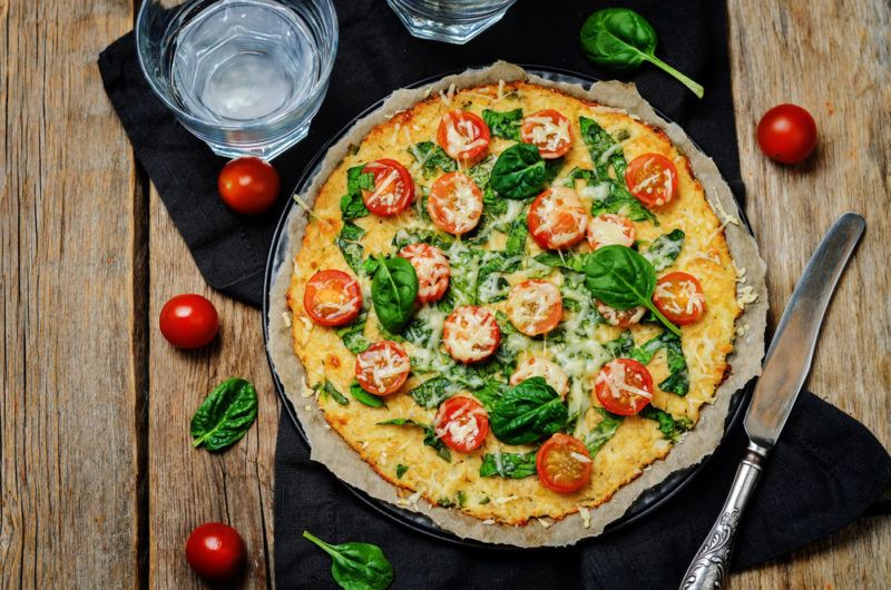 A cauliflower breakfast pizza on a black background