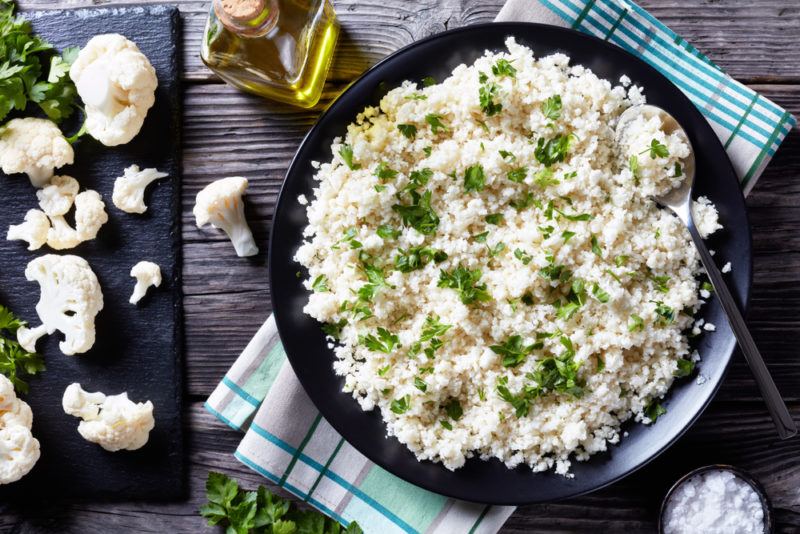 Cauliflower rice in a pan next to pieces of cauliflower