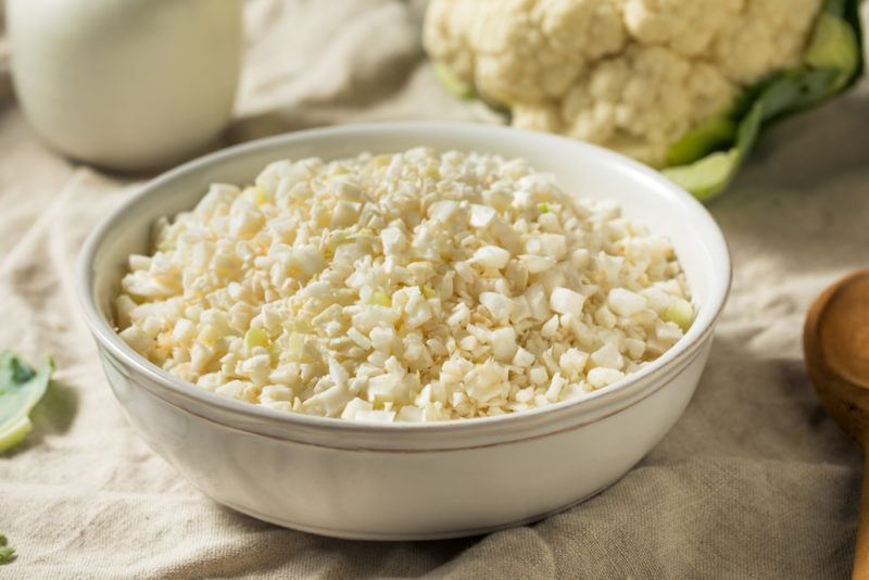 A bowl of cauliflower rice next toa cauliflower