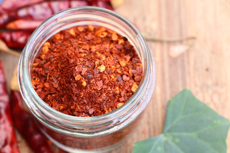 top view image of a jar full of cayenne pepper powder on top of a wooden surface with dried cayenne peppers