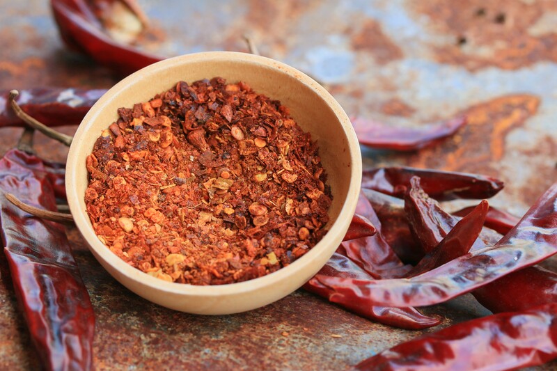 Small wooden bowl full of crushed cayenne pepper with dried cayenne peppers around it.