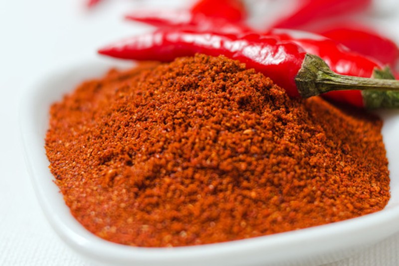 a white dish with a mound of cayenne powder with a couple of fresh cayenne peppers on top