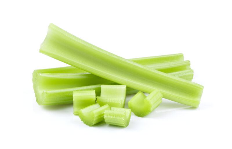 Three celery sticks and some chopped celery rest against a white background.